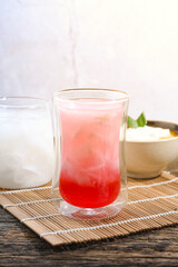 a glass of coconut water with red syrup on a wooden table. Coconut water can prevent vomiting and treat dehydration. Ramadan iftar meal