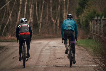 Gravel bike riding in rainy weather. Bikerider from behind wearing a safety helmet. Modern bicycle.