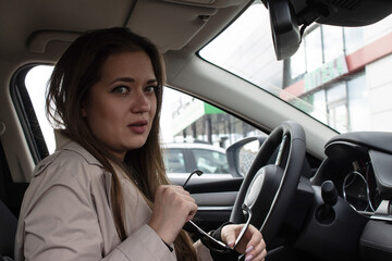 Portrait of a young brown-haired beautiful girl with green eyes and a light trench in the car