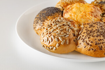 Loaf of bread from spherical buns with sunflower seeds, poppy, flax, cheese, on white plate, side view, space to copy text, selective focus.