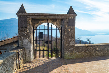 Ancient iron gate in a frame made of stone at the summit of Monte Isola (Mount Island), in the middle of Lake Iseo, Italy. Aerial landscape with italian alps and blue waters on the background.
