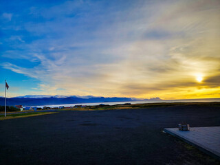A panoramic view of Iceland's rocky landscape, with the sun casting a golden glow over the ocean,...