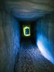 Obraz premium A narrow, illuminated ice tunnel inside Langjökull Glacier in Iceland, showcasing textured ice walls and a distant light at the end