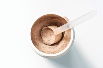 Chocolate protein powder in a scoop against plastic jar on white background.