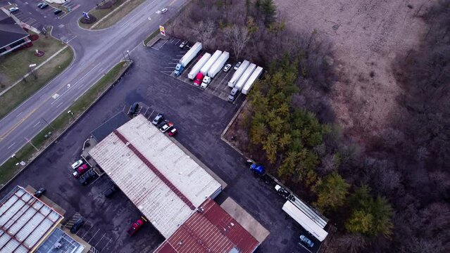 unique aerial above small truck stop parking lot with semi trucks, dry vans and reefers parked next to highway. top down drone 4k USA