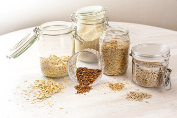 Cereals and seeds such as oat flakes, linseeds, sesame and sunflower seeds in glass jars on a...