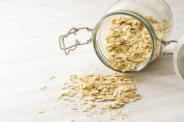 Oat flakes falling from a glass jar onto a light wooden table, healthy eating, copy space, selected focus