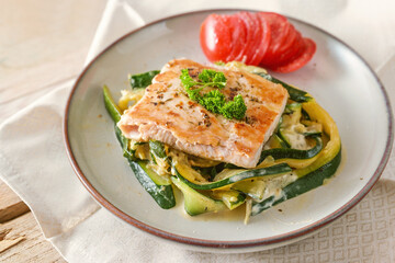 Fried wild salmon with parsley garnish on zucchini vegetables and fresh tomato on a light plate, healthy meal for a low carb diet, selected focus