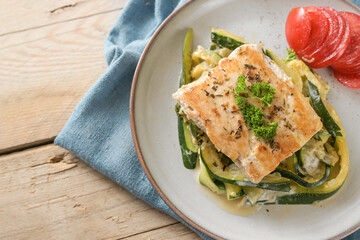 Roasted wild salmon fillet with parsley garnish on creamy zucchini vegetables and fresh tomato on a light plate, healthy meal for a low carb diet, high angle view from above, copy space