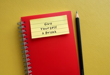 Note stick on red notebook with handwritten text GIVE YOURSELF A BREAK, concept of self compassion - self reminder to treat yourself as you would a friend with kindness and understanding