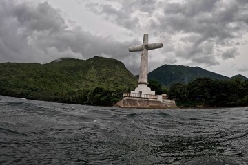 The cross of the sunken cemetery of Camiguin in the Philippines, located in the middle of the sea, in the background green hills.