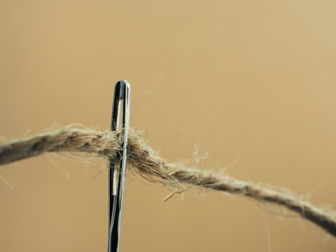 Aguja de coser enhebrada con cuerda .close-up de aguja aislada sobre fondo beige. concepto de costura