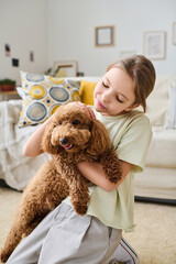 Vertical image of little girl embracing her cute dog and playing with it in the room at home