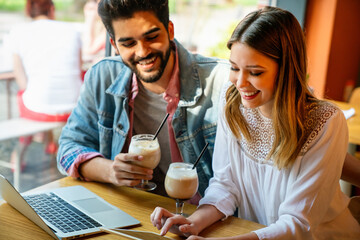 Couple sitting at cafe smiling, using laptop, spending time with pleasure, drinking coffee.