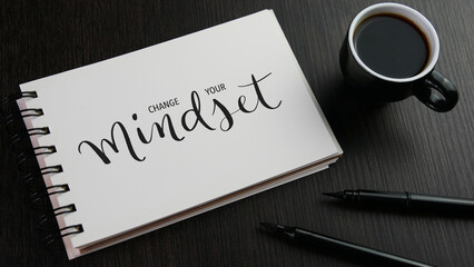 CHANGE YOUR MINDSET black lettering in notebook with cup of coffee and pens on black wooden desk