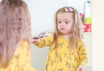 A girl with Down syndrome looks at herself in the mirror. The child smiles at his own reflection....