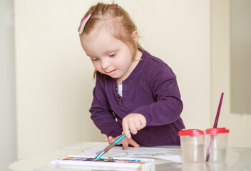 A girl with Down syndrome draws in an album with watercolors. Child development through creativity....
