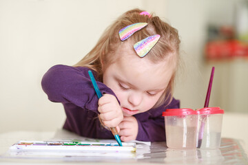 A girl with Down syndrome draws in an album with watercolors. Child development through creativity....