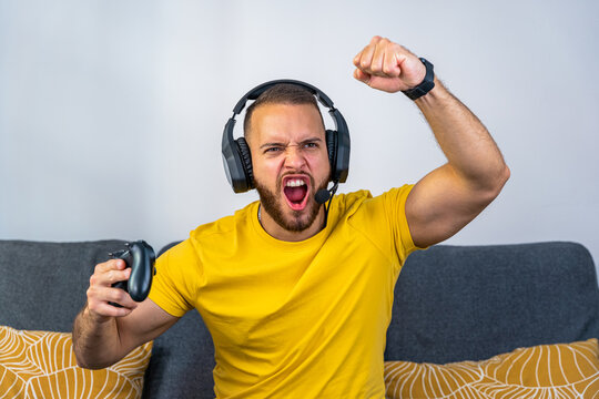 chaval euf&oacute;rico celebrando victoria gaming con mando de v&iacute;deo consola en mano y cascos gaming puestos - camiseta amarilla