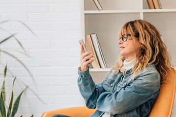 middle-aged woman on the sofa at home looking at the mobile phone