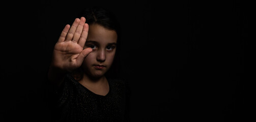 little girl with a raised hand making a stop sign gesture on a black background. Violence, harassment and child abuse prevention concept.