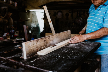 latin senior man carpenter using electric circular saw for cutting wooden boards, on a piece of wood in workshop in Mexico Latin America, hispanic people