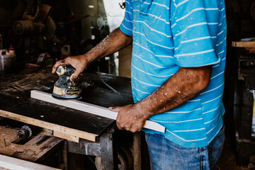 latin senior man carpenter using sandpaper on a polished wood in workshop in Mexico Latin America