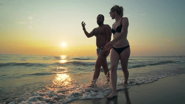 Young couple in love walking along coastline during sunset on tropical vacation. Slow motion