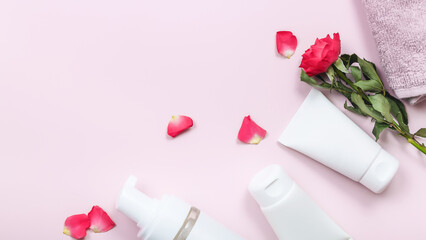 Composition with skin care products and rose flowers on pink table background. Copy space