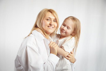 Portrait of a blonde mother and daughter who having communicate and play on a white background. Mom and little girl models pose in the studio. The concept of love, friendship, caring in the family