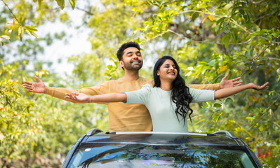 Happy smiling couple feeling nature fresh air by stretching arms on car sunroof - concept of togetherness, weekend holidays and refreshment - obrazy, fototapety, plakaty