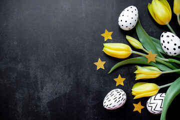 bouquet of yellow tulips and white easter eggs, coffetti stars in gold color on a black background. top view. copy space