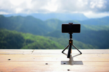 Wooden table balcony with fresh atmosphere in the morning, natural landscape. Focus on phone and tripod with blurred background