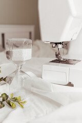 A sewing machine with an hourglass stands on a table, a light background. Content for seamstresses, sewing studios, fashion designers, handicrafts
