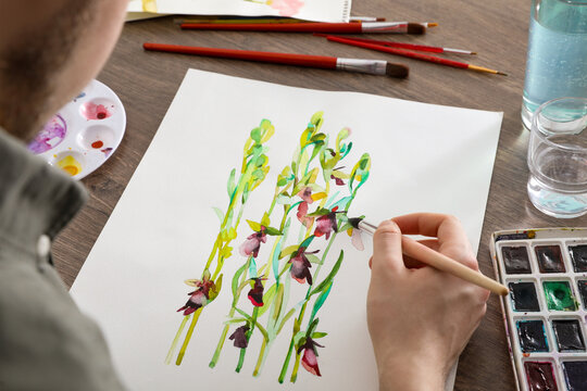 Man painting flowers with watercolor at wooden table, closeup. Creative artwork