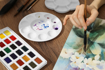 Woman painting flowers with watercolor at wooden table, closeup. Creative artwork