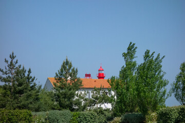 une maison au toit de tuile devant un phare avec des arbres