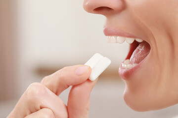 Woman putting chewing gum pieces into mouth on blurred background, closeup