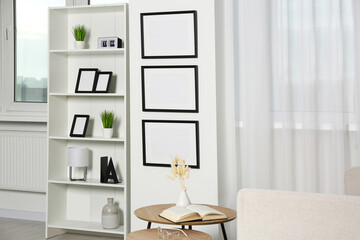 Stylish room interior with empty frames hanging on white wall near shelving unit