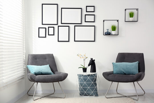Stylish room interior with empty frames hanging on white wall and comfortable furniture