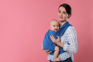 Mother holding her child in sling (baby carrier) on pink background. Space for text