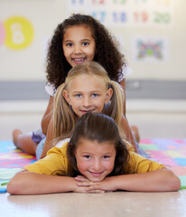 School kids, lying together and pile on floor, portrait and classroom for smile, solidarity or...