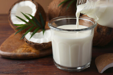 Obraz na płótnie Canvas Pouring delicious coconut milk into glass on wooden table