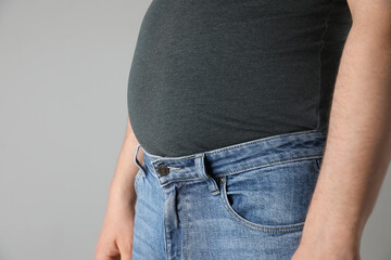 Overweight man in tight tshirt and jeans on light grey background, closeup. Space for text