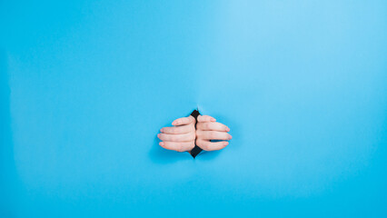 Female hands sticking out through a hole on a blue background. 