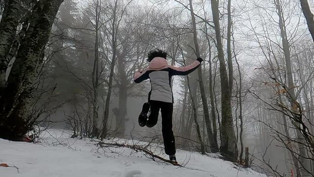 Scared woman running away through the snow covered forest, looking back to see if someone if chasing her. Slow motion