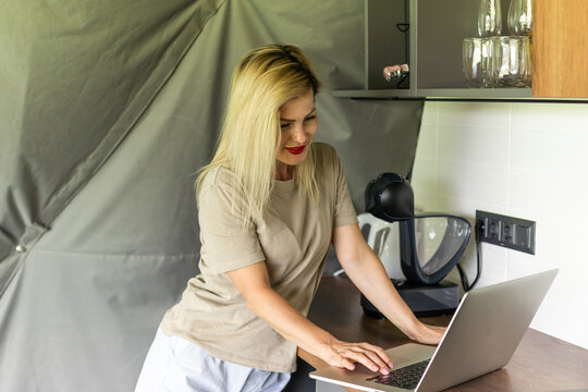 Portrait Of A Cheerful Woman At Home With A Laptop And A Cup Of Coffee On The Table. 30 Year Old Girl Connected Online To A Meeting With Friends And Family. Telework Concept.