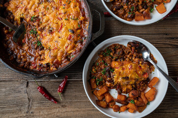 Bean stew with cheddar cheese, chili topping  and roasted sweet potatoes on wooden table from above