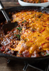 Bean stew alla chili con carne with cheddar cheese topping in a cast iron pan