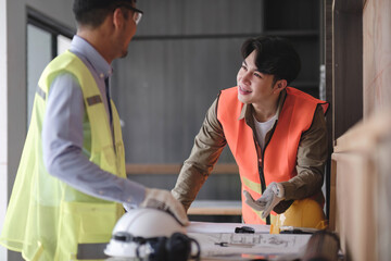Fototapeta na wymiar young man construction team engineer in vest and hat working with laptop standing on construction site House building project. Engineer talking with colleagues at work